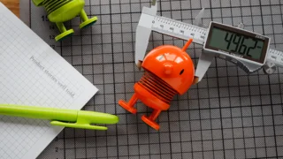 Büroartikel mit bunten Hoptimist-Figuren, einer digitalen Schieblehre und einem Stift auf einem Schreibtisch
