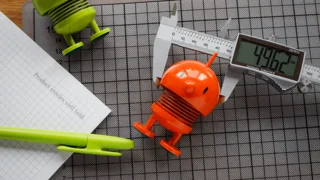 Büroartikel mit bunten Hoptimist-Figuren, einer digitalen Schieblehre und einem Stift auf einem Schreibtisch