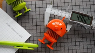 Büroartikel mit bunten Hoptimist-Figuren, einer digitalen Schieblehre und einem Stift auf einem Schreibtisch