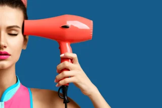 Eine junge Frau hält sich einen Haarfön seitlich an den Kopf.