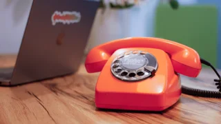 Telefon mit Wählscheibe, geöffneter Laptop mit Aufkleber Produktdatenliebe auf Displaydeckel