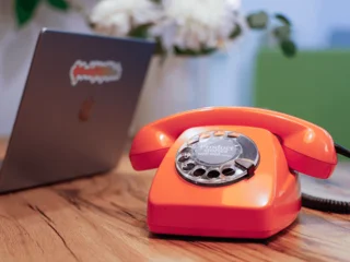 Telefon mit Wählscheibe, geöffneter Laptop mit Aufkleber Produktdatenliebe auf Displaydeckel