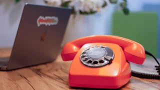 Telefon mit Wählscheibe, geöffneter Laptop mit Aufkleber Produktdatenliebe auf Displaydeckel
