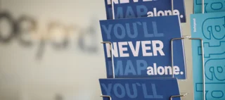 Kartenständer mit Postkarten mit Schriftzug: You`ll never map alone und forbeyond Schriftzug im Hintergrund